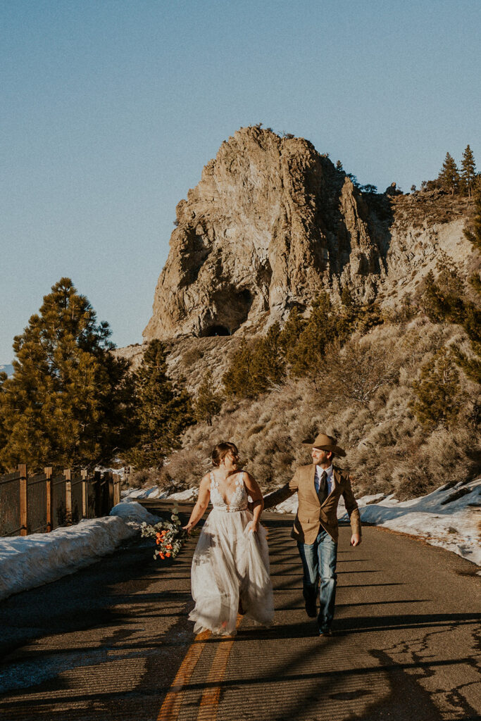 Man wearing cowboy hat and woman in white dress running on wedding day at Cave Rock Nevada