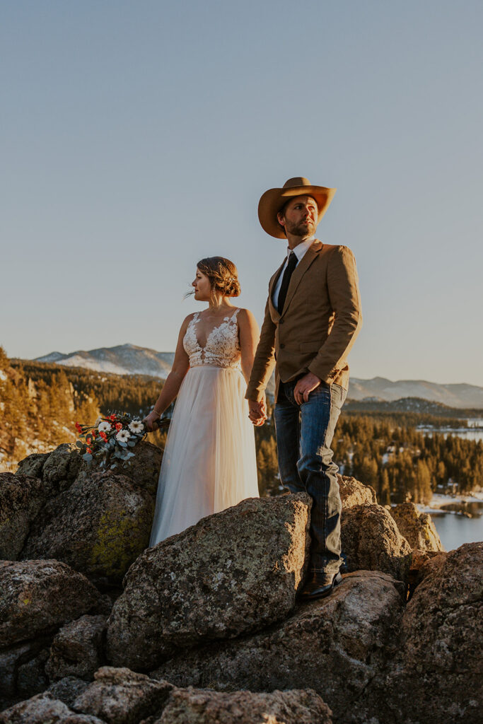 Man wearing cowboy hat and woman in white dress stand at overlook on wedding day at Cave Rock Nevada 