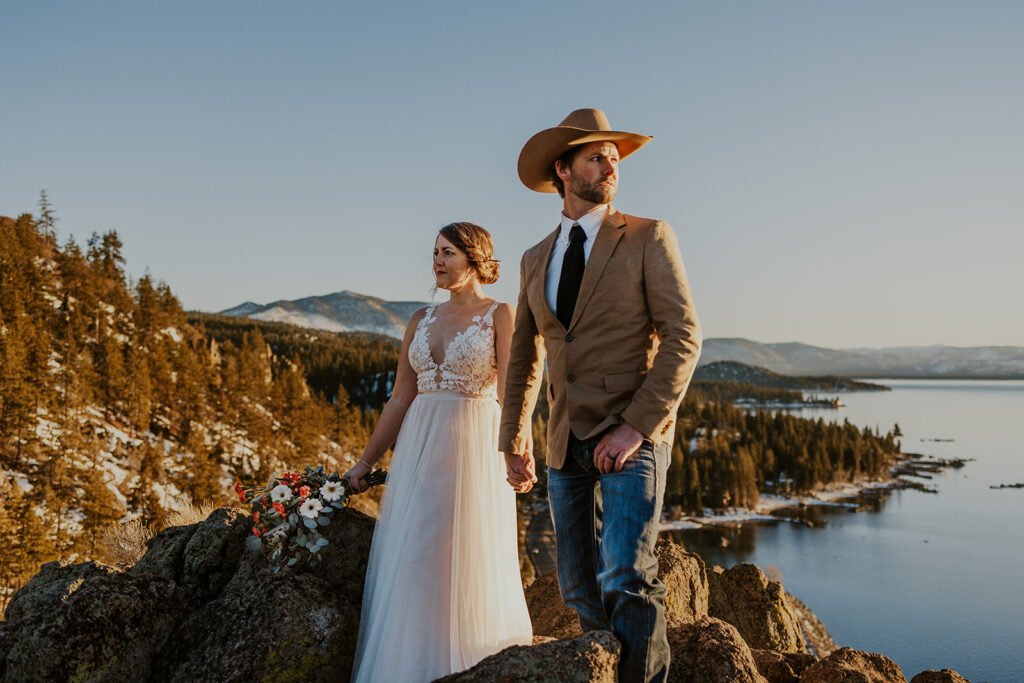 Man wearing cowboy hat and woman in white dress stand at overlook on wedding day at Cave Rock Nevada 