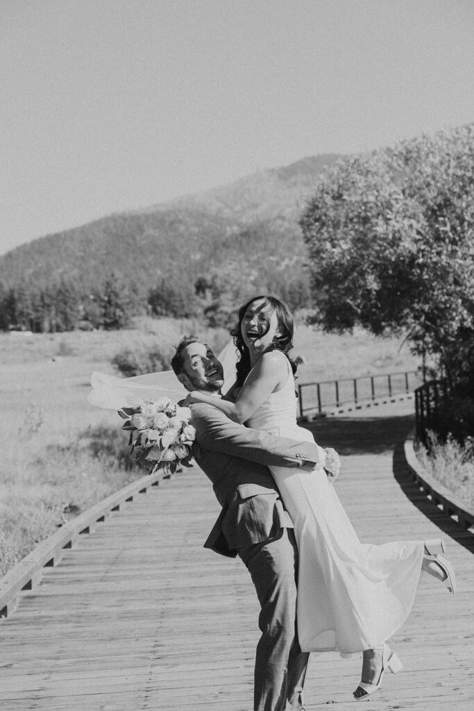 black and white photo of man and woman in white dress hugging on trail in woods of Khale Park Nevada